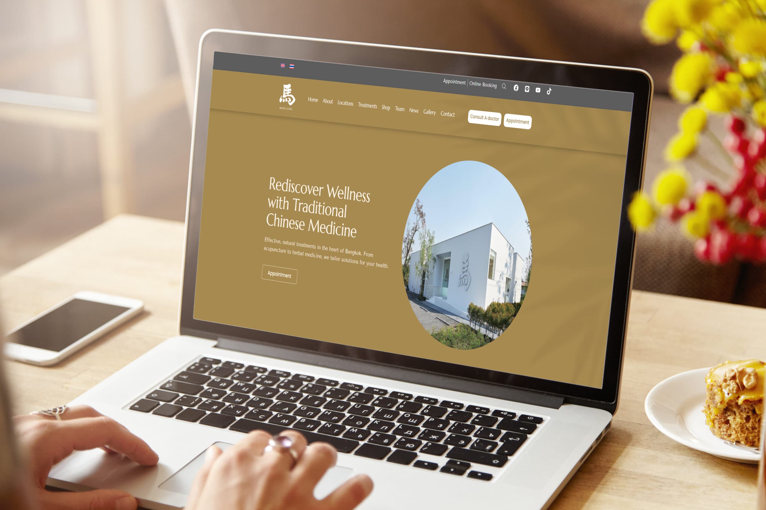 Woman’s hands typing on laptop keyboard with white blank screen with copy space for your advertising content, sitting at coffee shop table with mobile phone and cake next to her. Selective focus