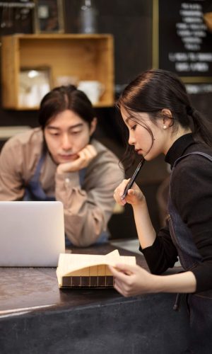 japanese-woman-reading-from-notebook-while-japanese-man-is-working-his-laptop-restaurant