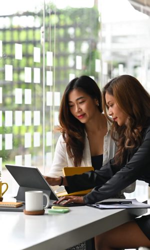 two-female-business-colleagues-working-together-computer-tablet-office